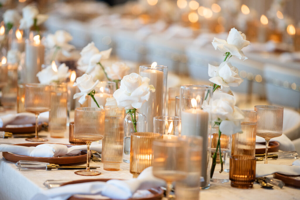 Table with bud vases with a single white rose, amber votive holders and beige pillar candles spanning the length of the table at the Riggs hotel  