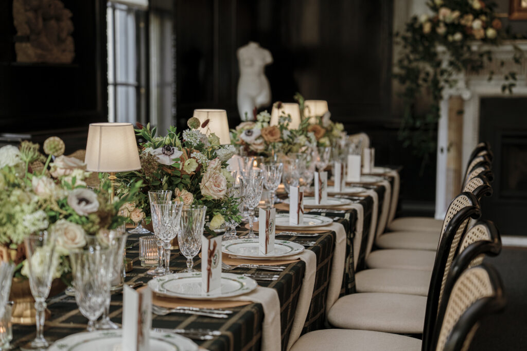 Rectangular table with white and ivory flowers, mini lamps, pillar and votive candles spanning the length of the table. 
